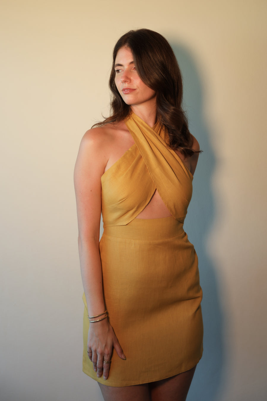 Woman wearing a mustard yellow halter neck dress against a plain background